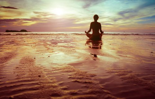 Women meditating with a sunrise sitting on the beach