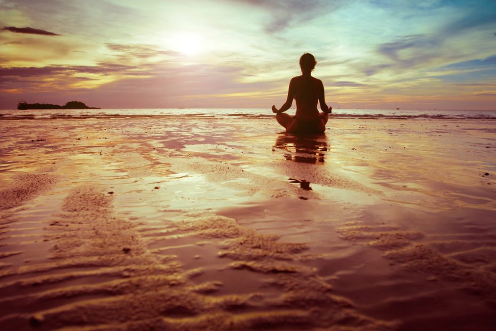 Women meditating with a sunrise sitting on the beach