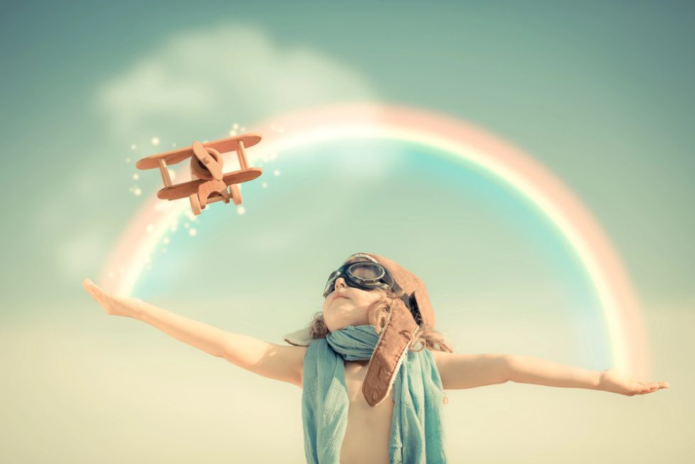 little girl under a rainbow flying a toy plane